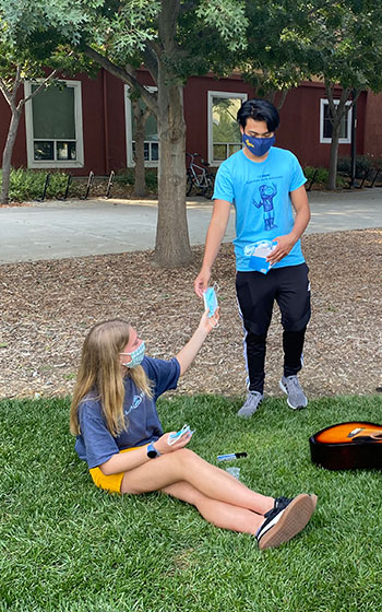 Student health ambassador give a face mask to another student