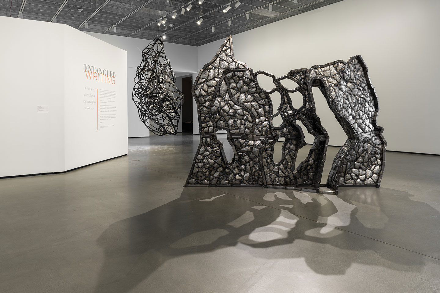 Installation view of sculptures of Beatriz Cortez’s steel sculpture “Adrift in a Mirrored Sea (Hansbukta),” 2024 (foreground) and Phillip Byrne’s “Before We Become Spirals,” 2024. Transoceanic aluminum-lined cable casings found in a Villeperdue recycling plant, earth residue, rivets, steel and zip ties.  Photo: Muzi Rowe