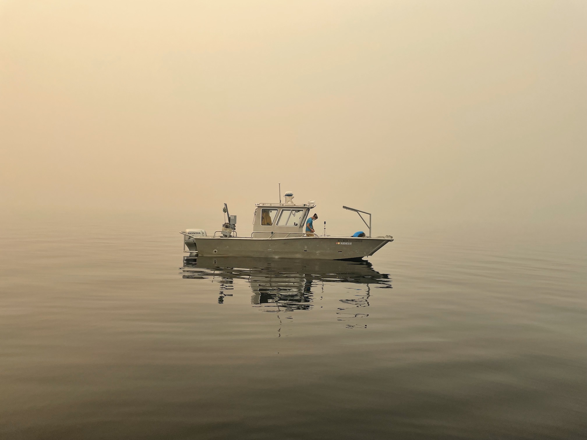 A reseach boat sits on Lake Tahoe duriign heavy beige smoke as scientists sample the water from the boat
