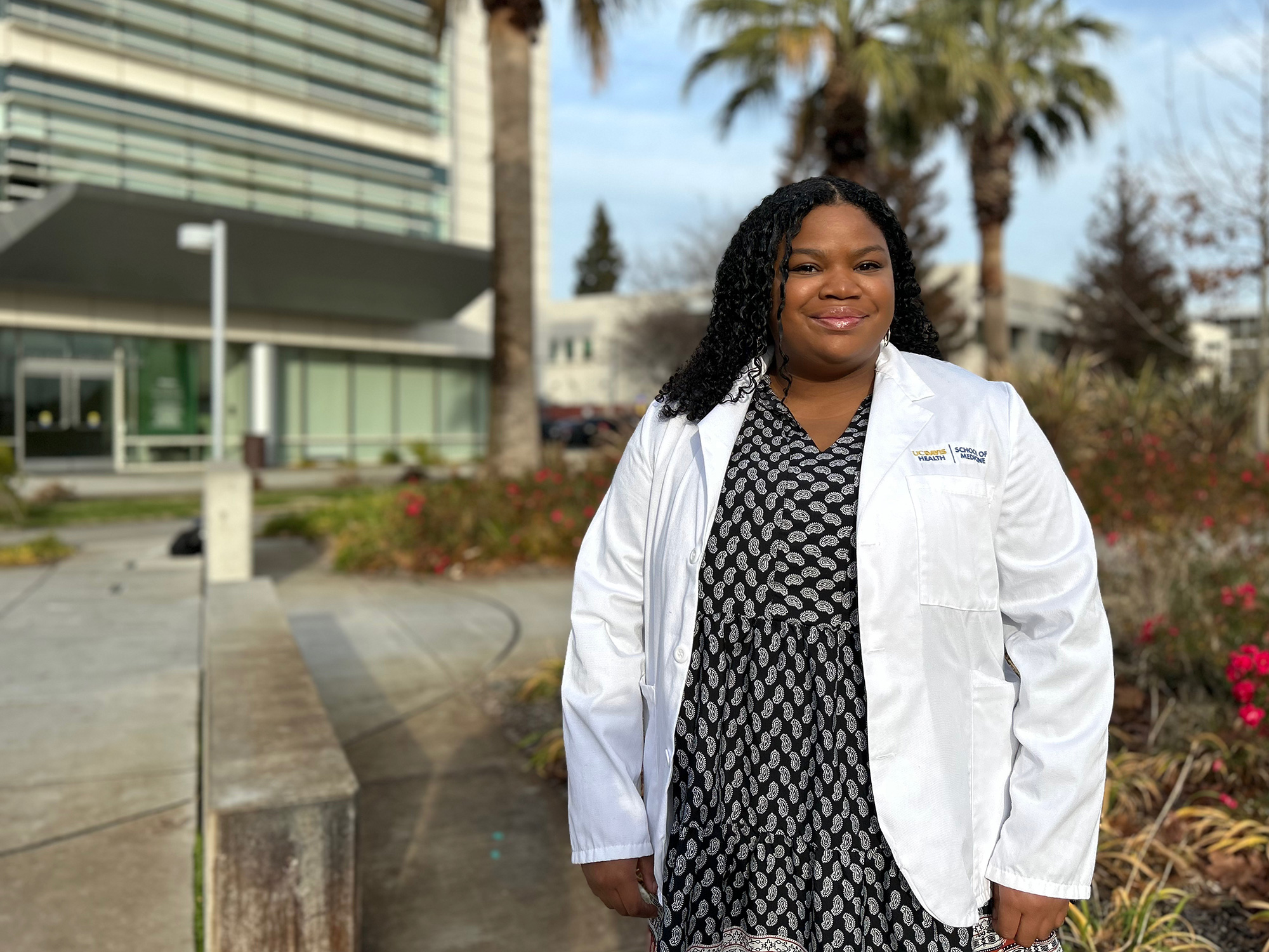 Medical student in a white coat stands outside 