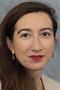 Headshot portrait of a woman with long brown hair, red lipstick, and small gold pearl earrings