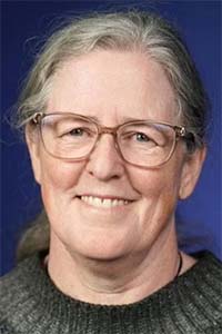 Smiling woman with glasses, gray hair pulled back, blue background