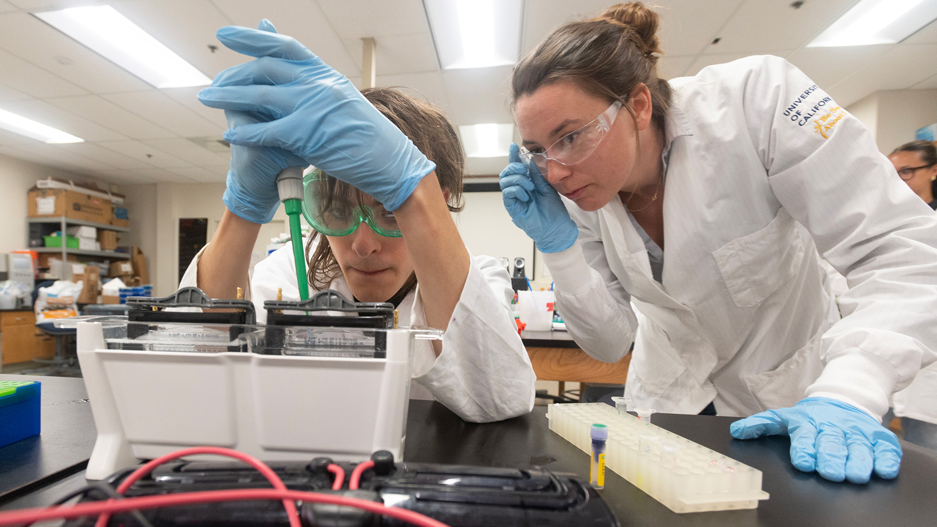 Two people in lab coats with pipette in lab environment