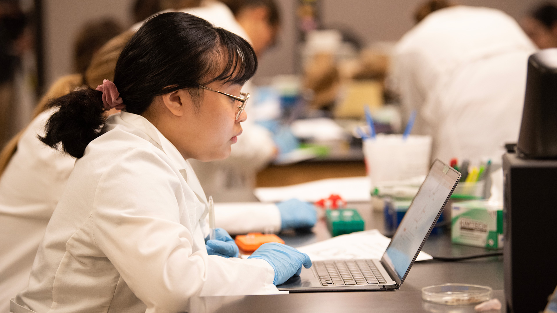 Student in a lab coat looks at a laptop