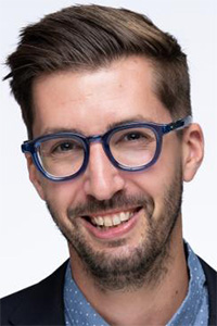 Headshot photograph, smiling man with blue glasses and short brown hair