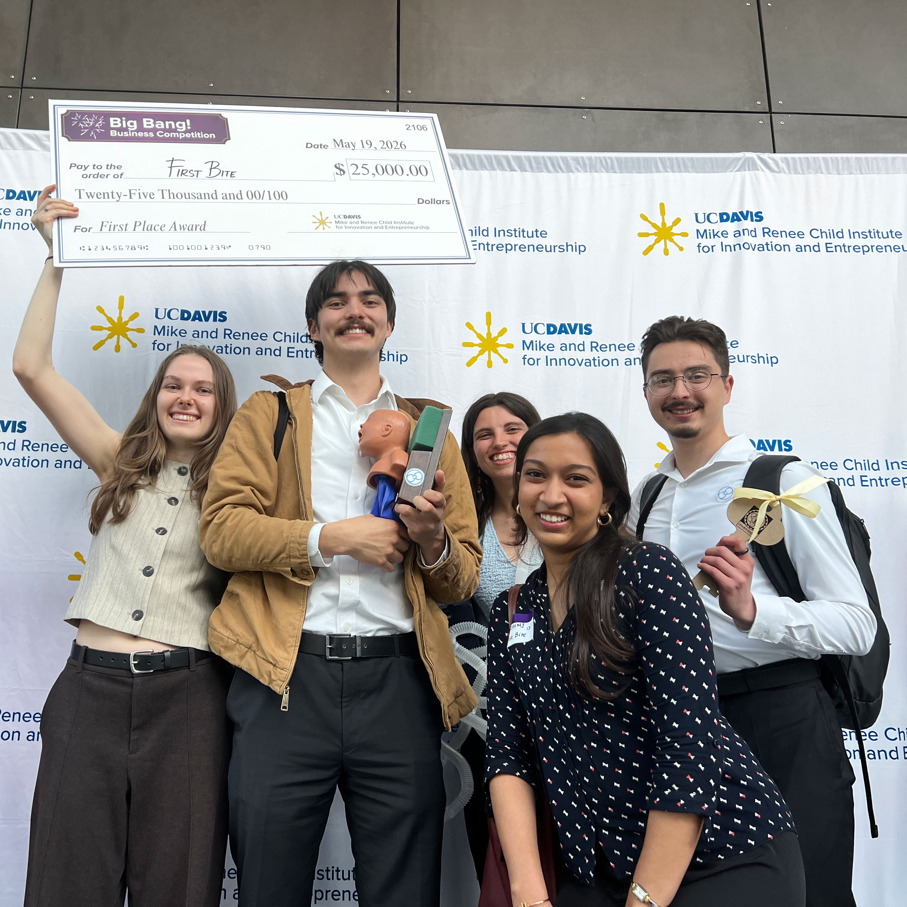 Group photo: five smiling people holding oversized check in front of UC Davis backdrop