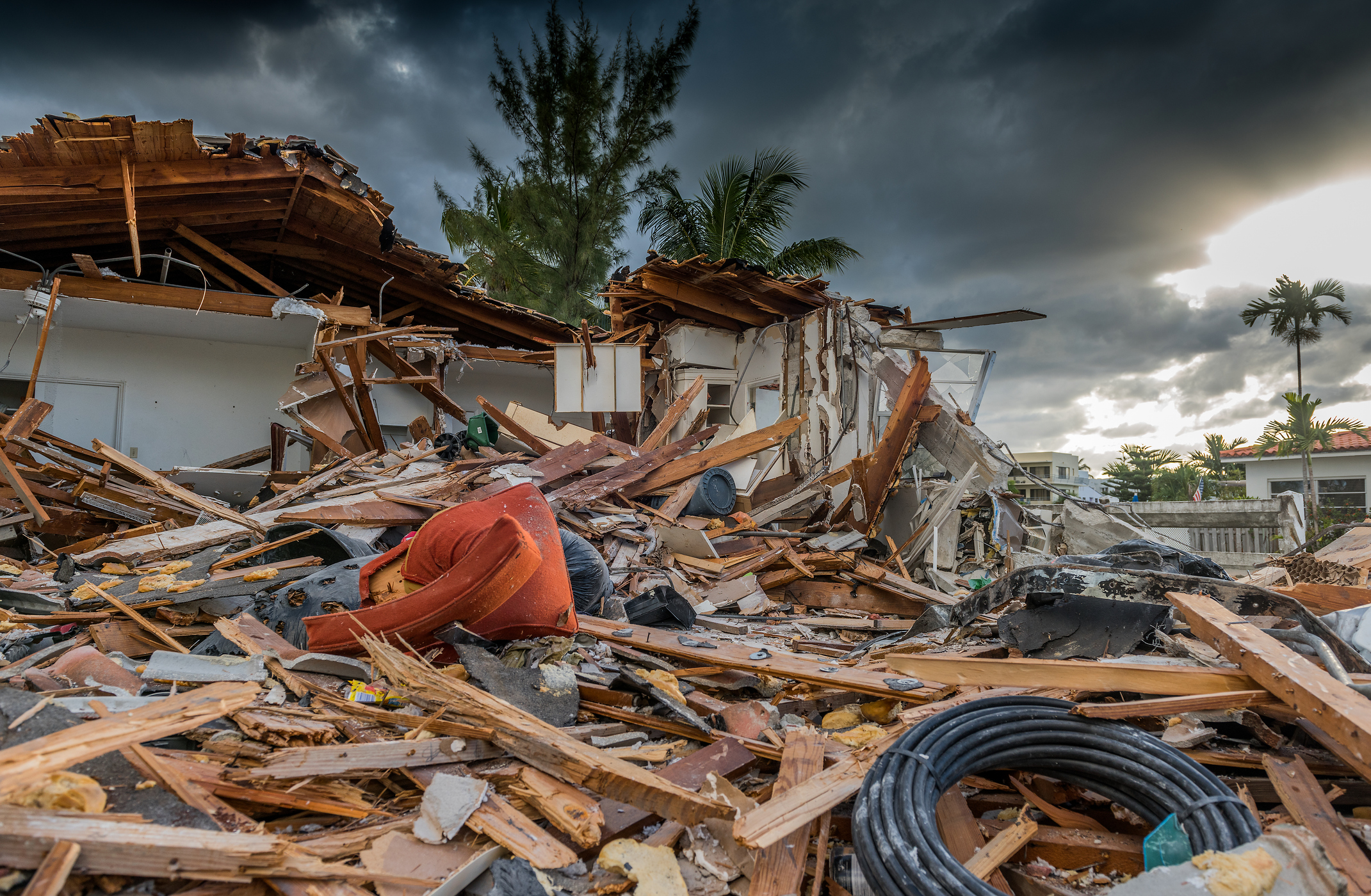 broken boards and trash beside damaged home under stormy skies following hurricane