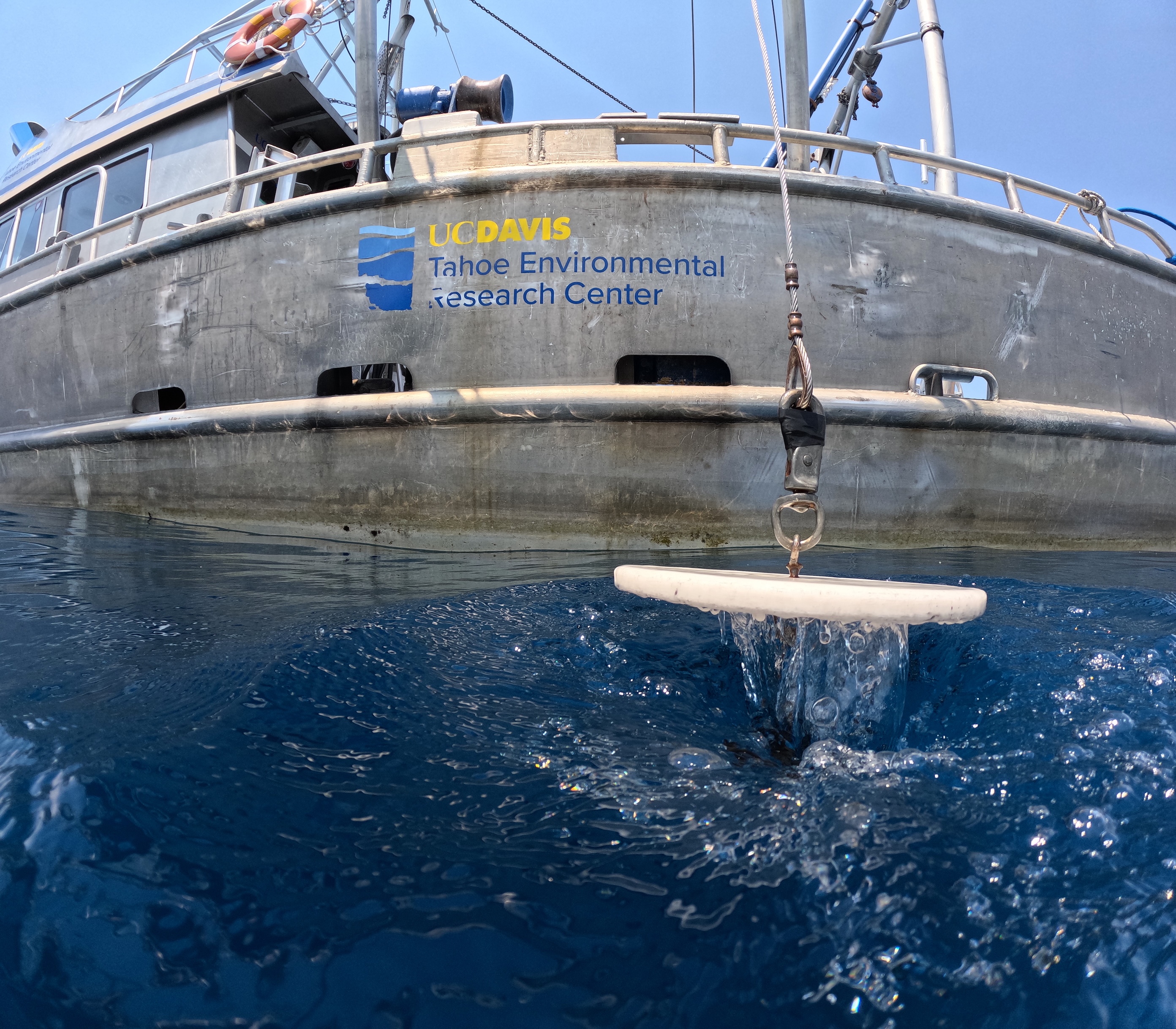 Research vessel hull labeled LV Davis lowering a white Secchi disc into deep blue Lake Tahoe