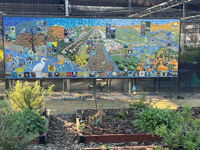 Colorful mural depicting plants, animals, and landscapes in a garden setting.