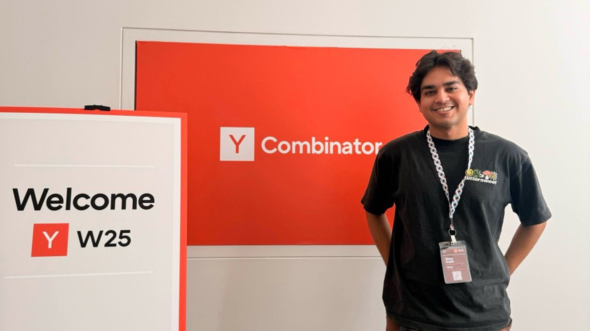 Smiling person with lanyard standing beside Y Combinator welcome signs