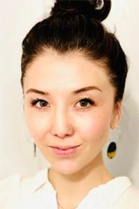 Woman with dark hair in a bun, subtle smile, white top and dangling earring