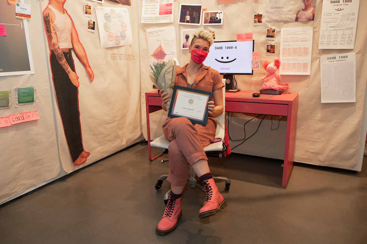 Artist with blond hair sits in front of exhibit at museum