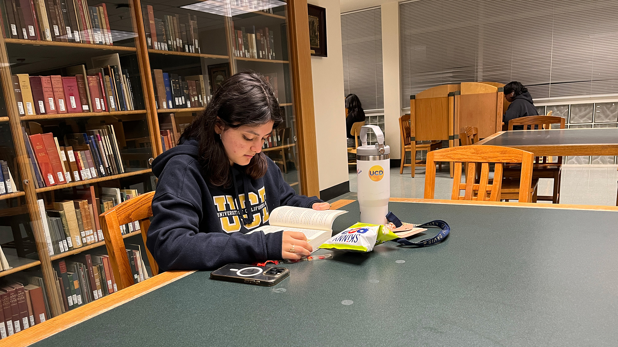 A UC Davis student reads a book at a table in the library