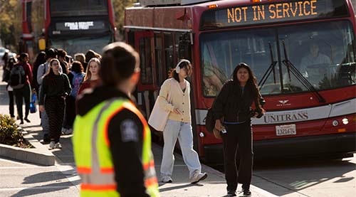 Crossing guard looks at crowd of students and Unitrans bus.