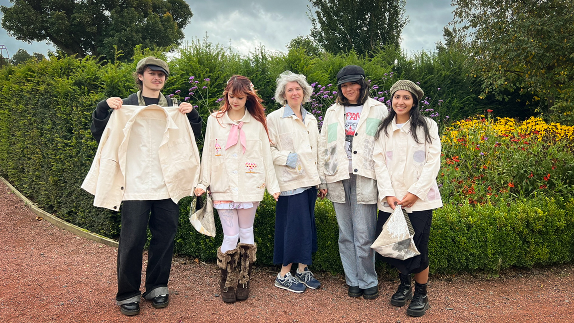Five individuals in matching outfits stand in a garden filled with colorful flowers.