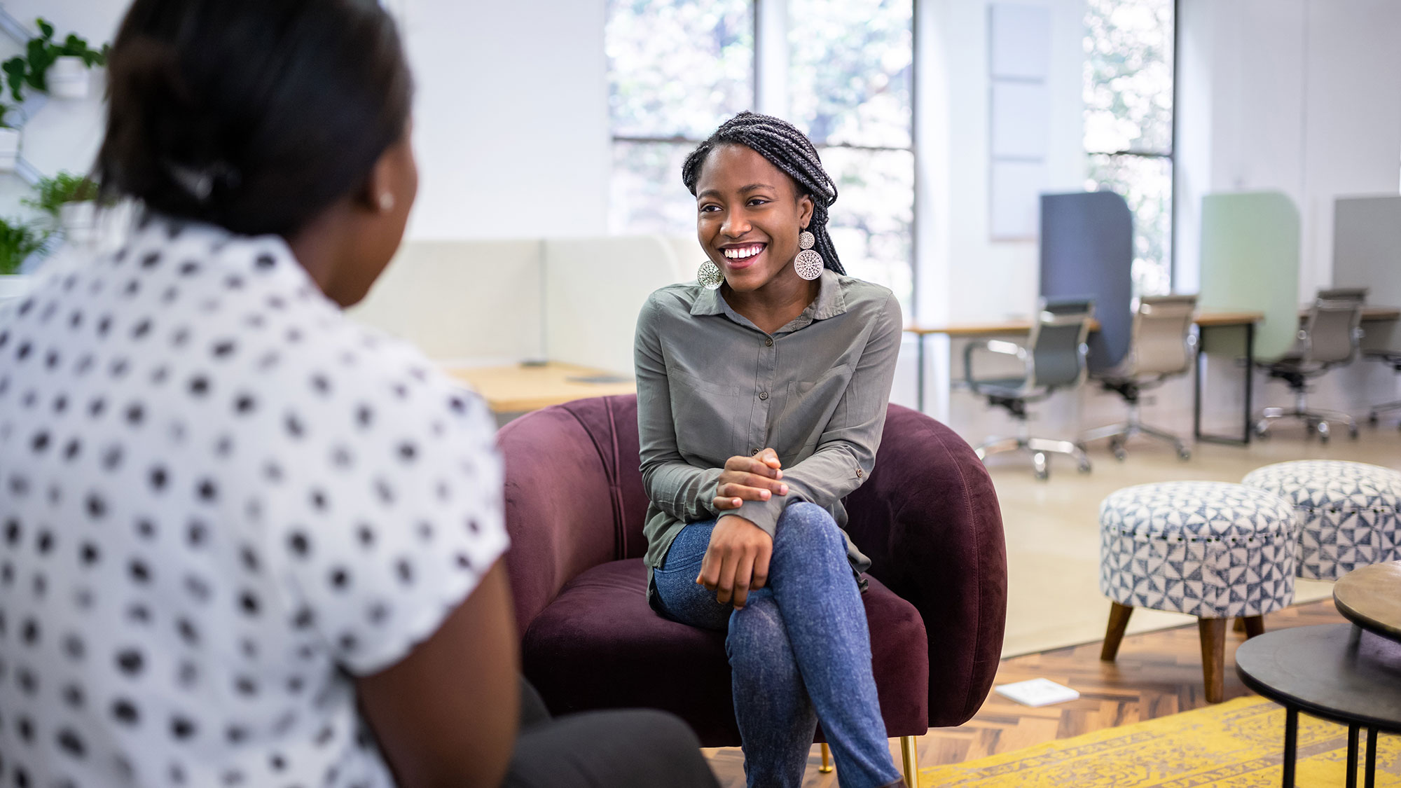 Smiling woman in grey talks with someone in bright office lounge.
