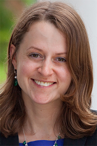 Smiling woman with shoulder-length brown hair, green earrings, blue top (photo)