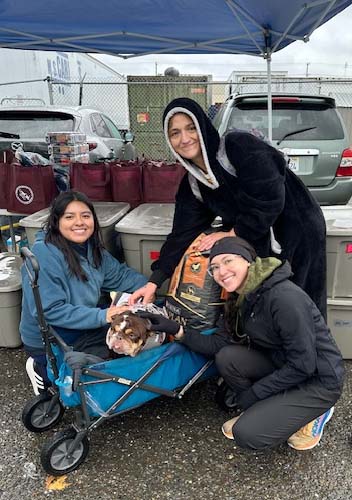 Three people pose for photo next to a dog who is sitting in a wagon