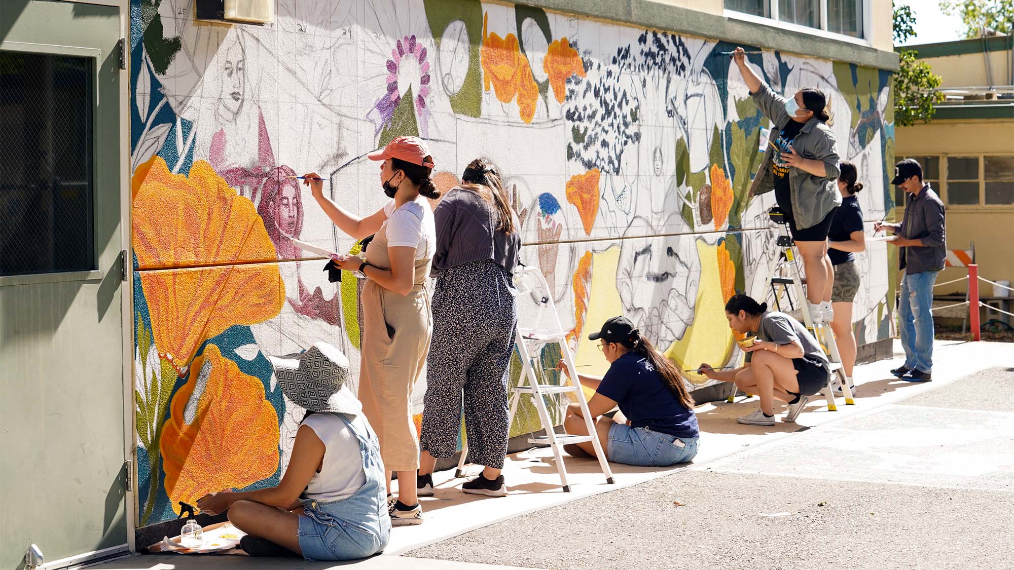 Students painting a mural on a wall at a school