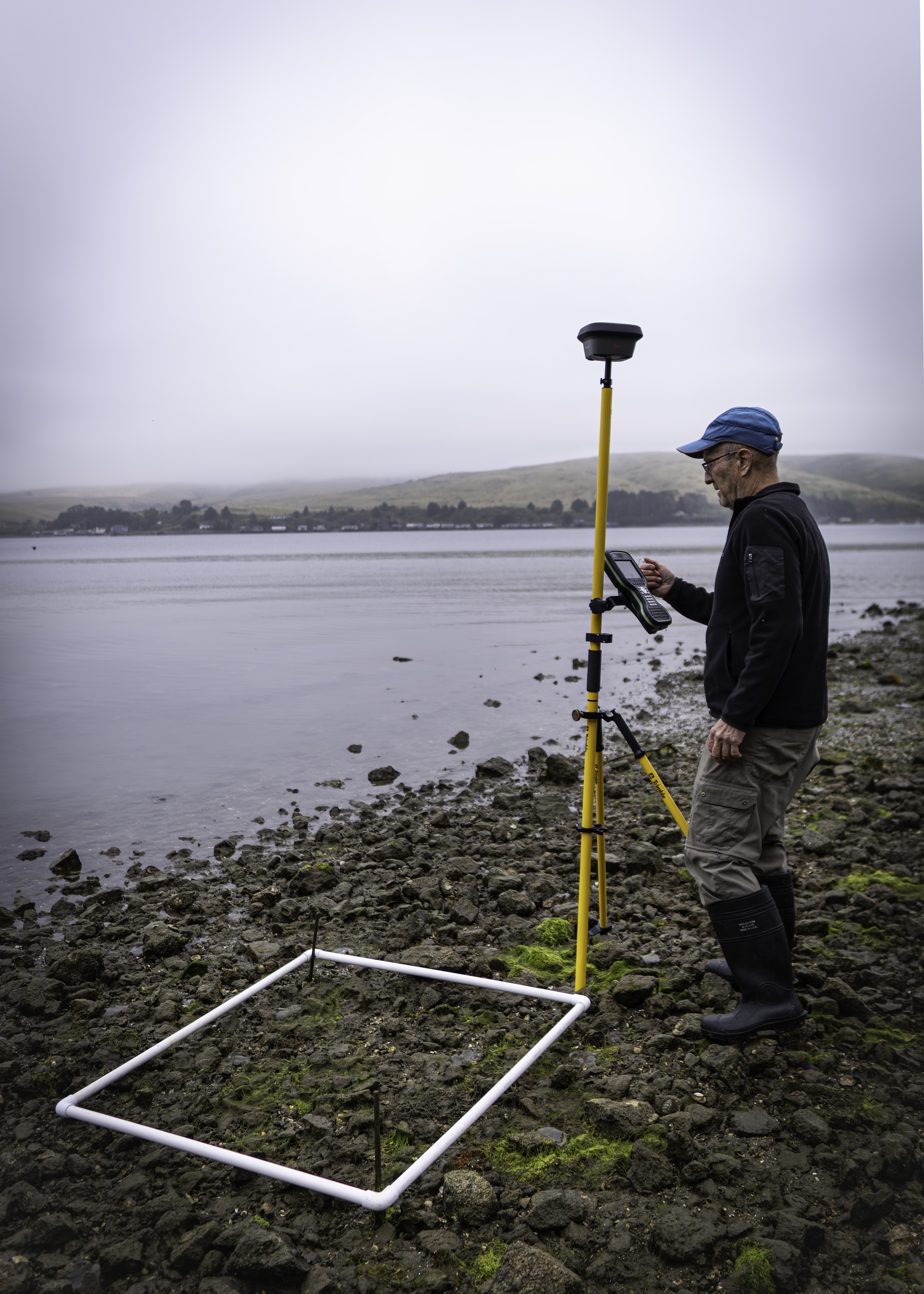 scientist Ted Grosholz in field clothing working with monitoring equipment along the edge of a rocky shore.