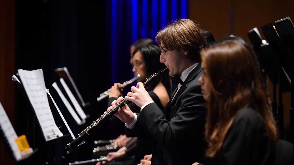 Three musicians in black formalwear playing flutes and clarinets on a dimly lit stage