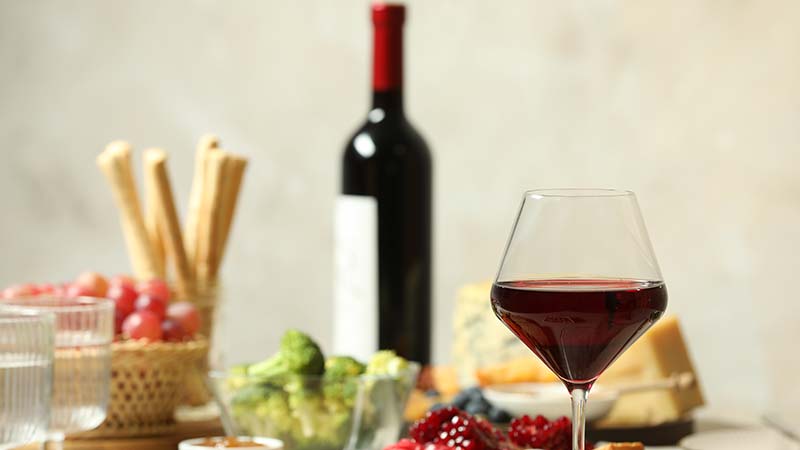 Photo of a table with wine in a glass, a wine bottle, breadsticks, fruit, and other appetizers.