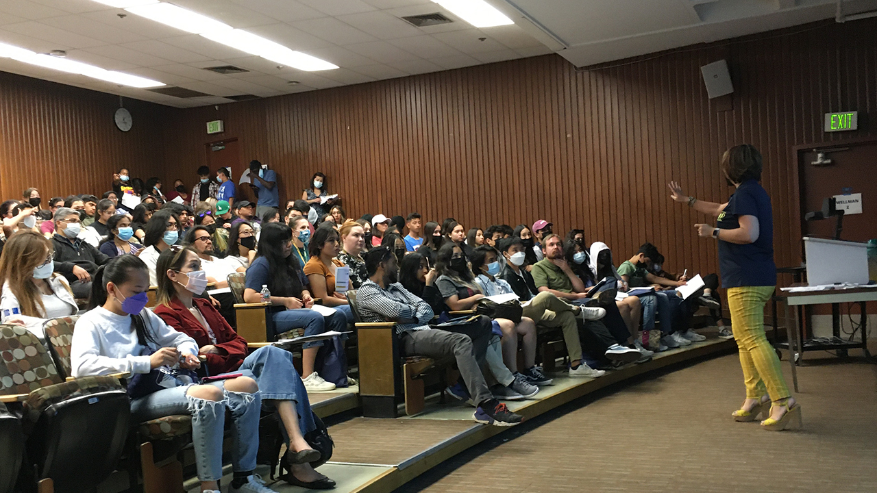 A standing woman talks with students seated in a tiered classroom