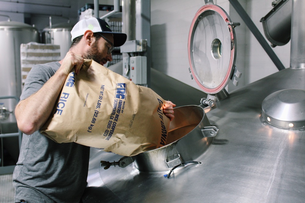 Man pours large bag of rice into brewer.