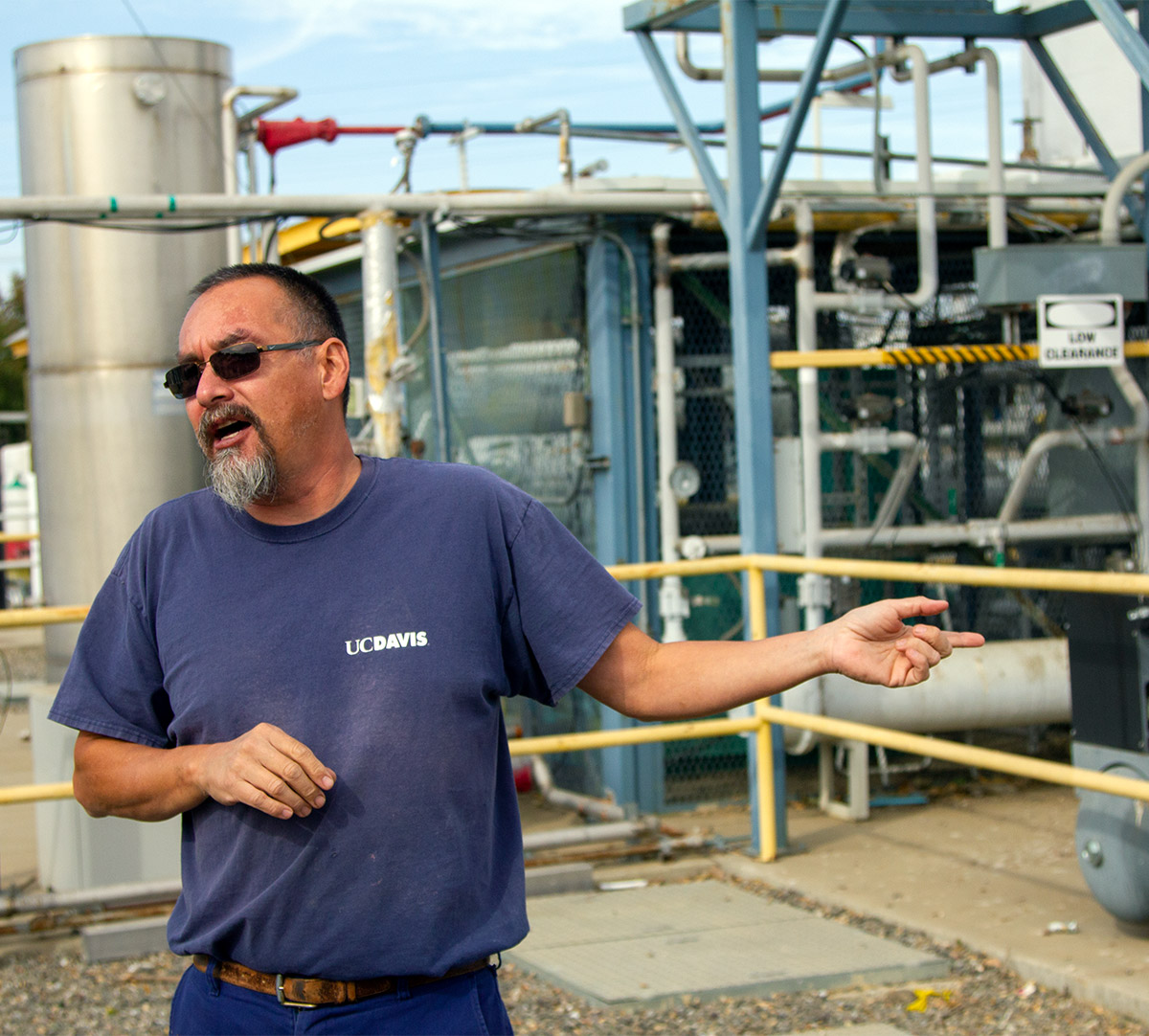 Man in blue T-shirt stands in front of machinery.