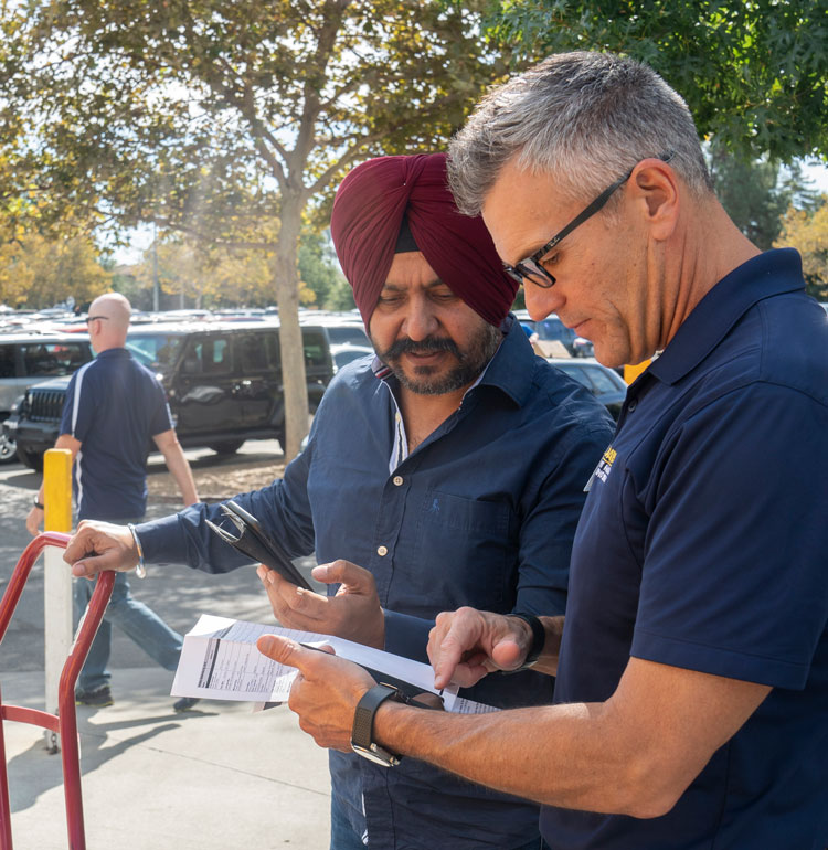 Mike Sheehan looks at a clipboard, to assist a parent standing next to him on Move-In Weekend..