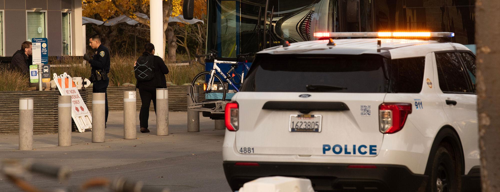 A campus police officer speaks to a student outside of his police car