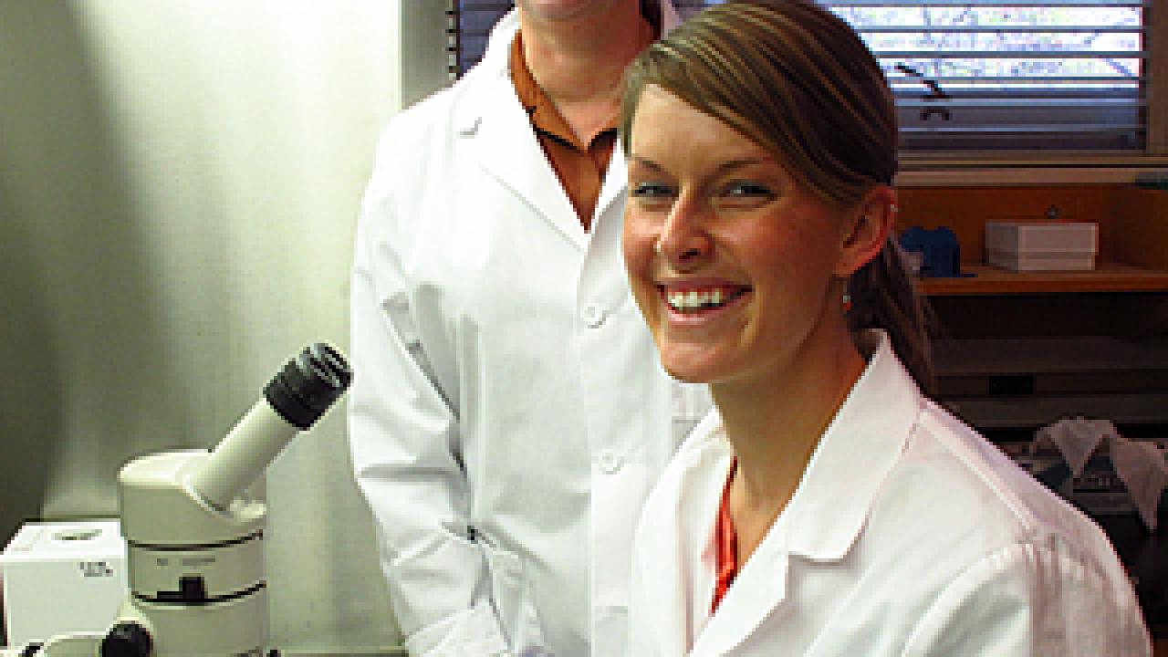 Paula Goines sitting at microscope with Pamela Lein standing behind