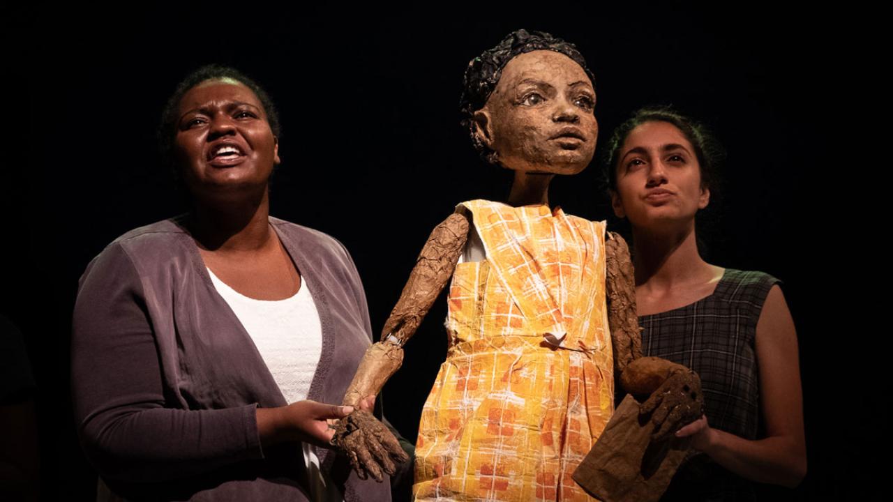 Student actors flank puppet.