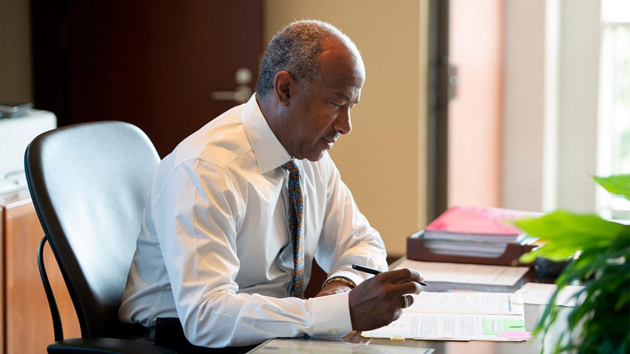 Chancellor Gary S. May writes at a desk.