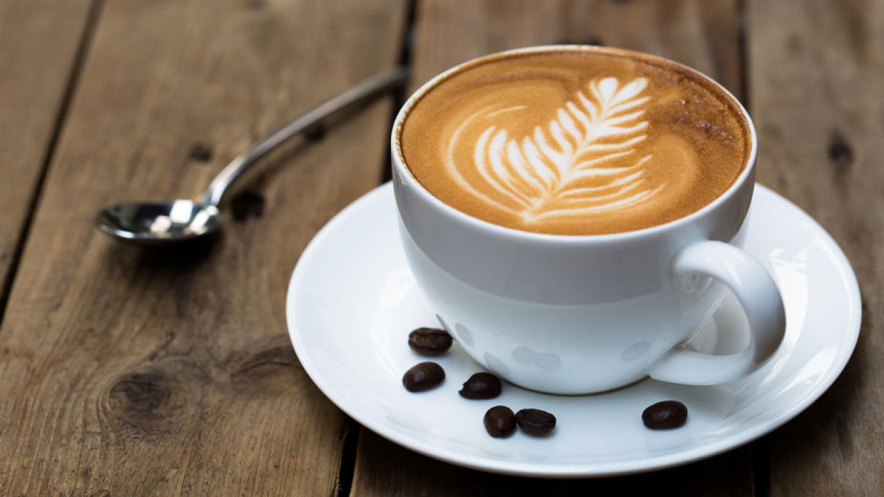 Cup of frothy coffee with design on top, beans in saucercoffee 