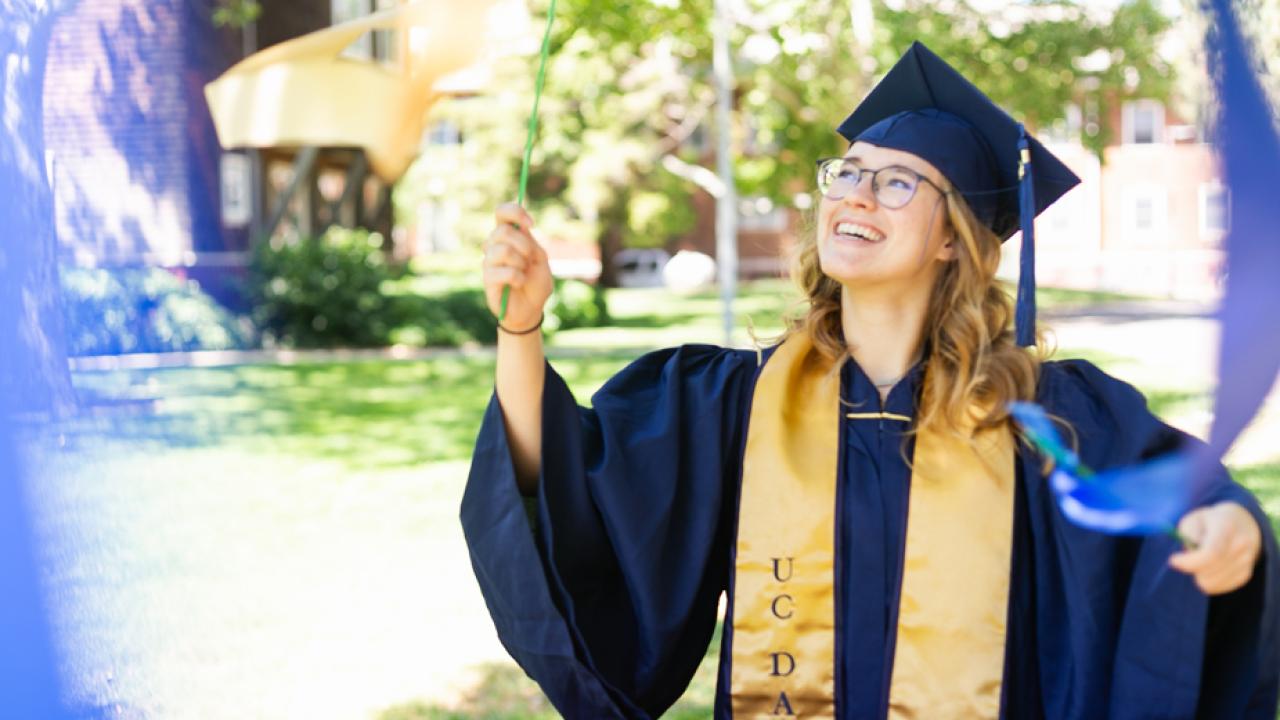 Kendal Hicks in cap and gown, waving blue and gold ribbon wands