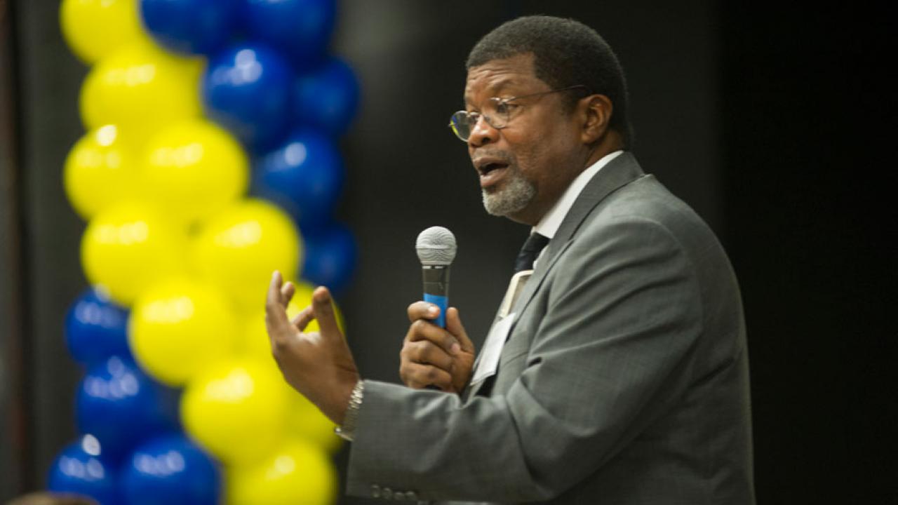 Walter Robinson speaks from podium, with backdrop of blue and gold balloons.