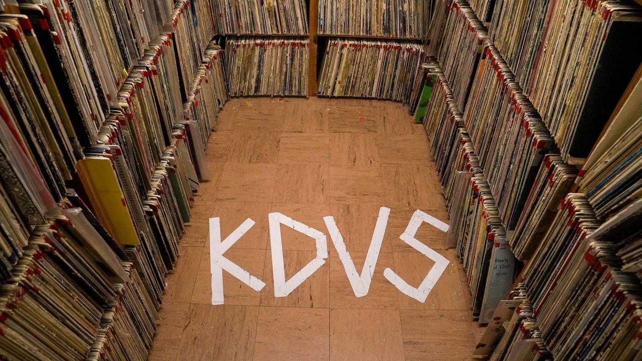 Photo: stacks of records with KDVS spelled on the floor with tape