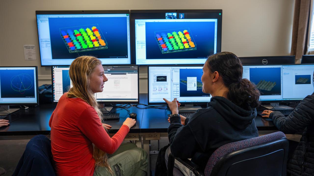 Two women engaged in discussion at computers displaying colorful 3D graphics. UC Davis students Jasmin Baptista and Kaia Broomell examine LiDAR data collected from an orchard canopy as part of a course in Unmanned Aerial Systems.  (Jael Mackendorf/UC Davis)