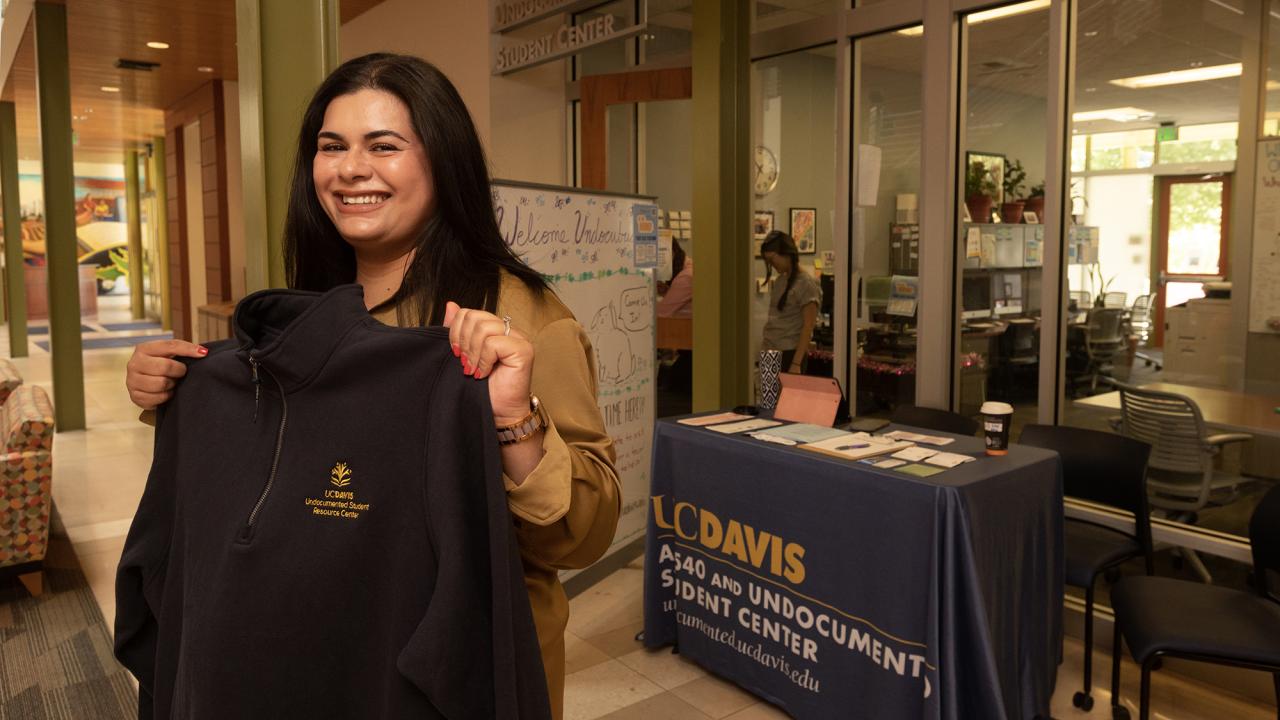 Audirana holds up a sweatshirt with the new logo of what is now known as the Undocumented Student Resource Center