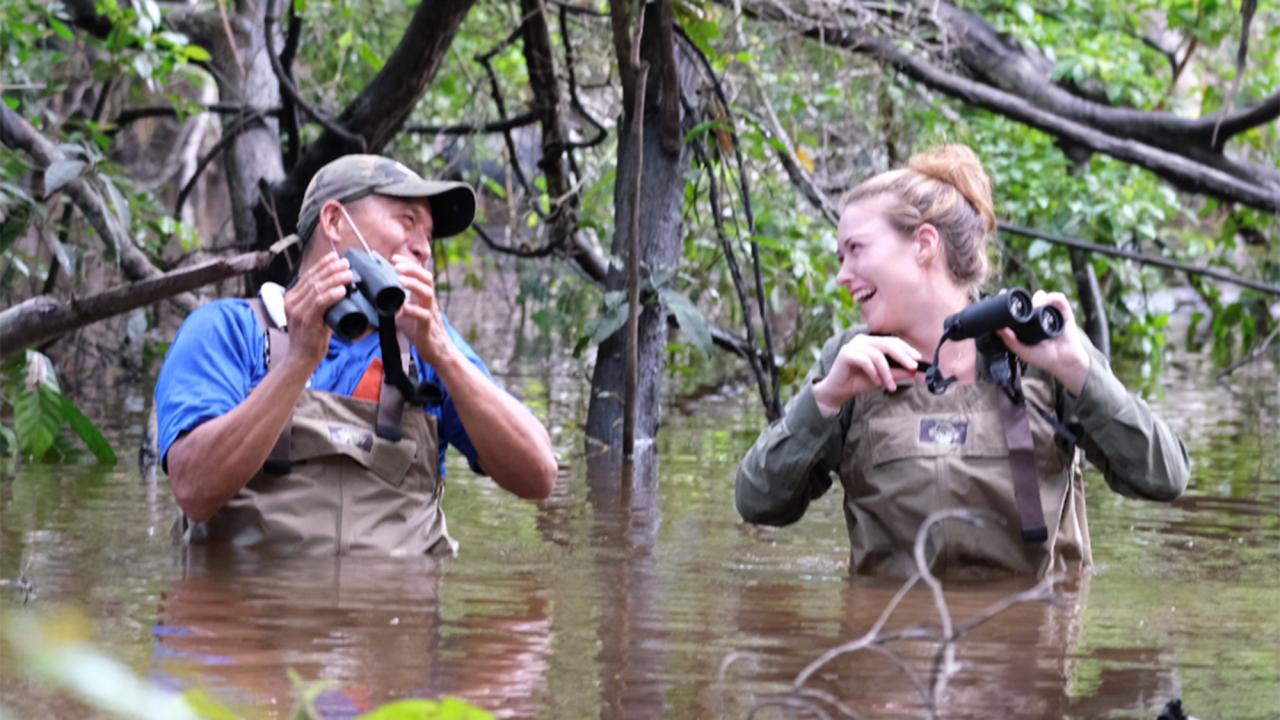 Two people are chest deep in flood waters in the Amazon rainforest.
