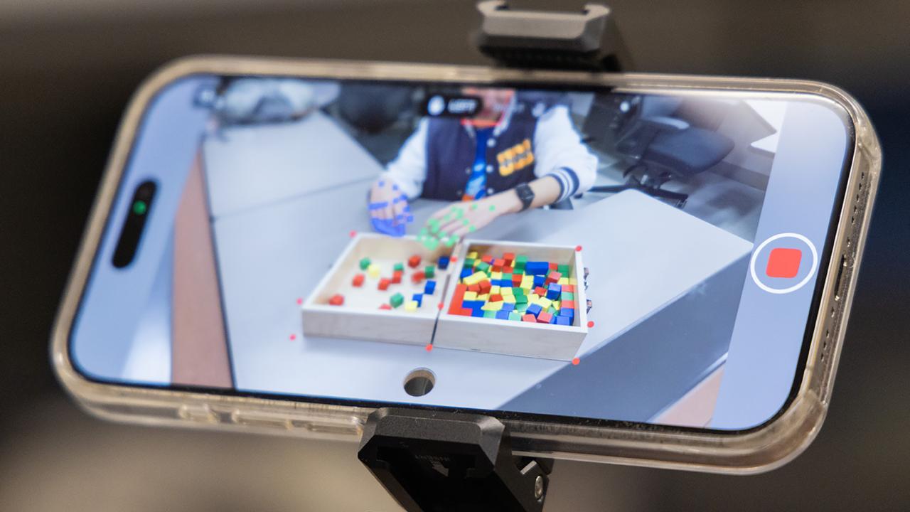 A smartphone displays a hands-on activity with colorful blocks on a table.