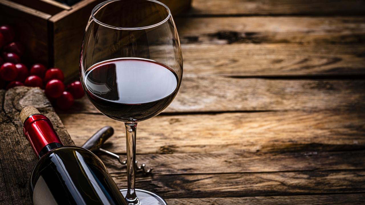 Close up view of a red wineglass shot on rustic wooden table. A wine bottle is laying beside the wineglass. Selective focus on the wineglass. A corkscrew, grapes and a wine bottle box complete the composition. (Getty)