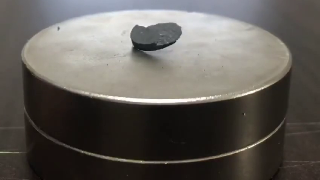 Pellet of grey stone-like material hovers in the center of a shiny metal disk. 