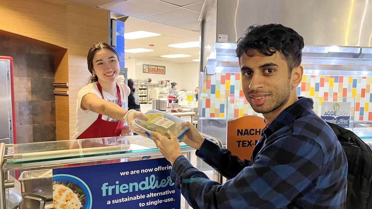 A Coffee House worker serves food in a blue reusable container to a student at UC Davis. 