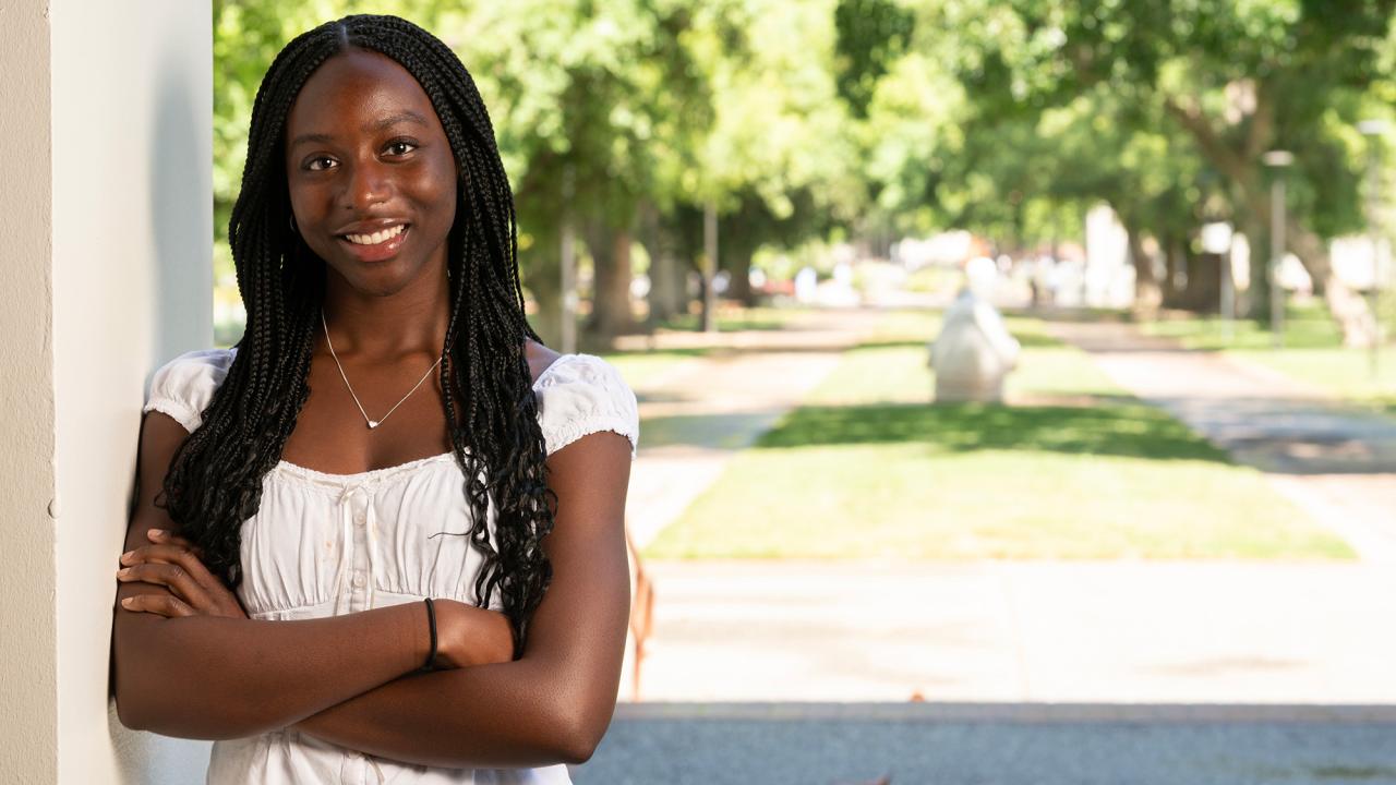 Student stands with her arms crossed with campus in the background
