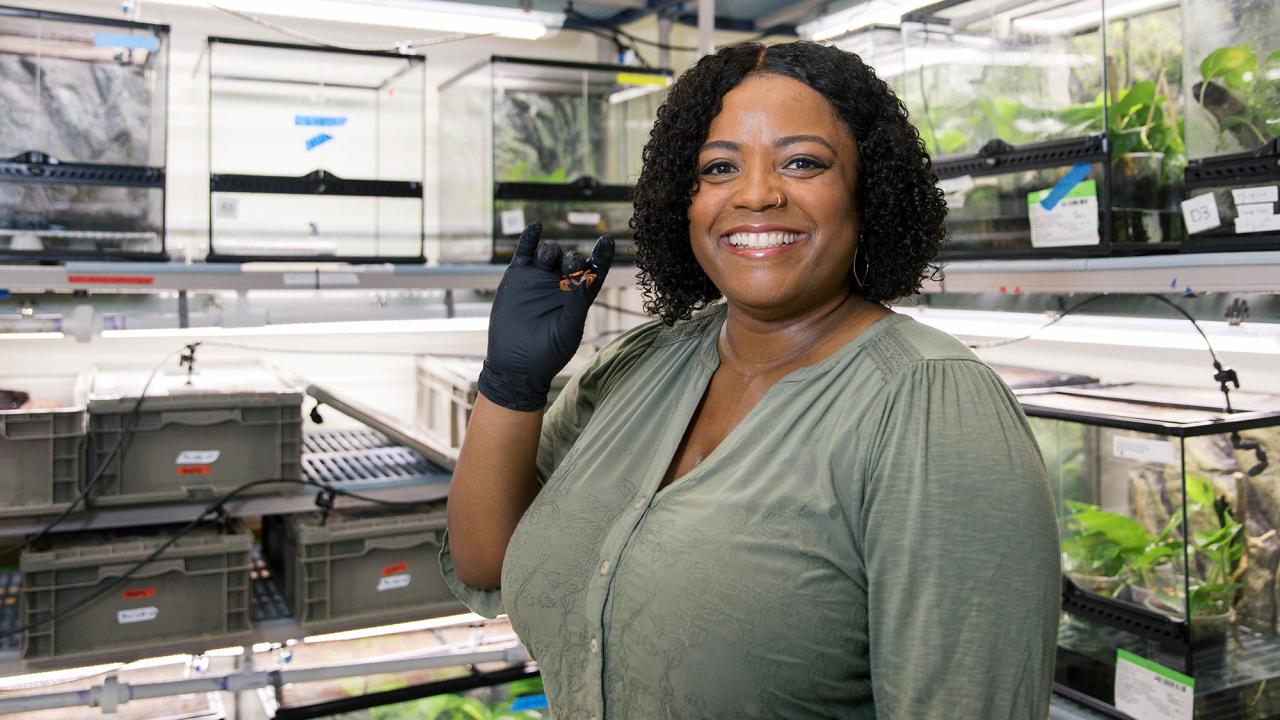 Woman stands in a lab and holds up a small crab in her right hand