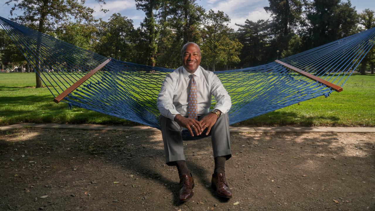 Chancellor Gary S. May, in shirt and tie, seated on hammock, on the Quad.