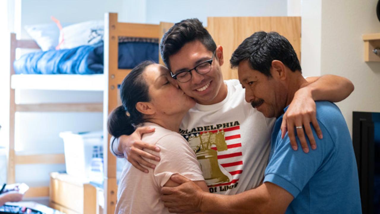 a student hugging his parents inside a residence hall room