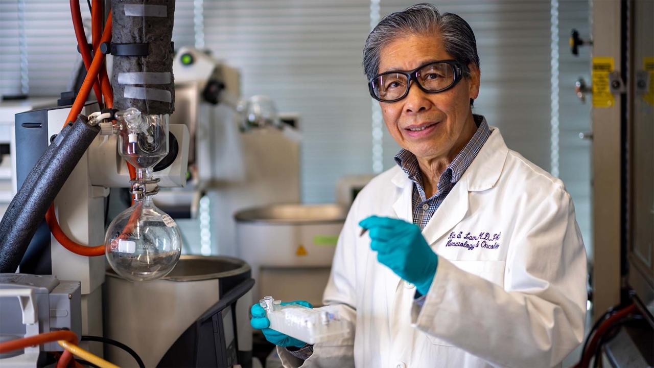 Smiling scientist in a lab coat and teal gloves holding a vial in a laboratory photo